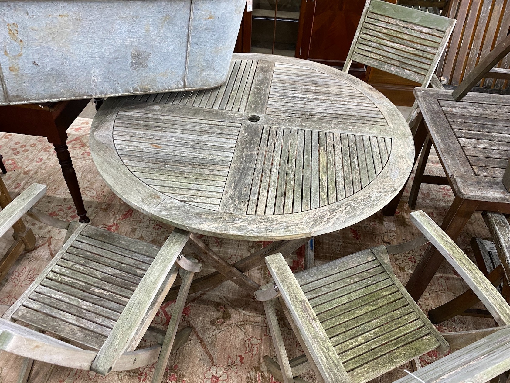 A John Lewis retailed weathered teak circular folding garden table, diameter 120cm, height 74cm and four folding elbow chairs, two with arms